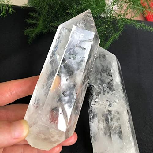 Två klara kvarts kristaller hålls upp av en hand.