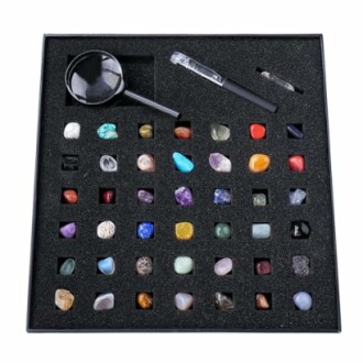 Olika ädelstenar i en låda med förstoringsglas och verktyg.