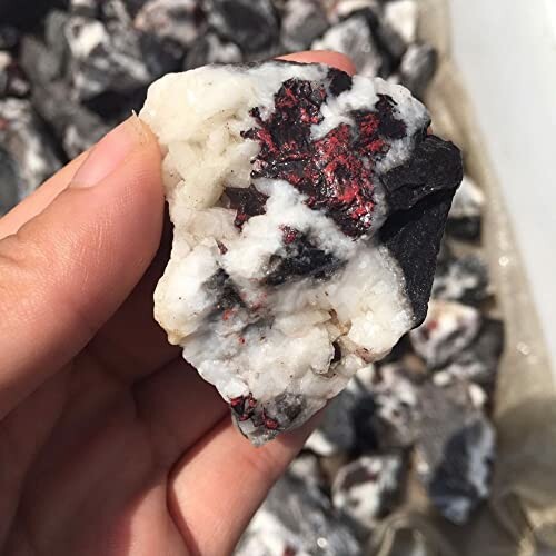 Hand håller rå mineralsten med vita och röda inslag