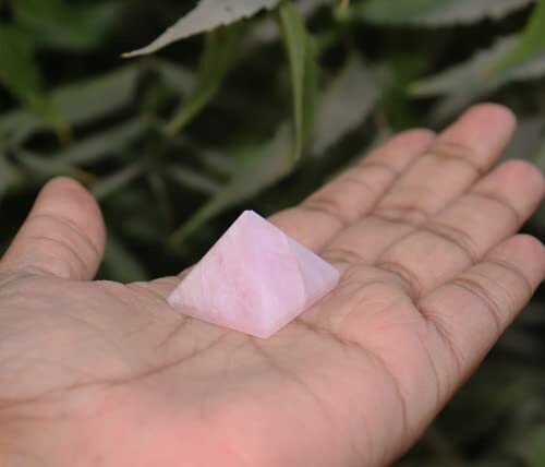 En hand håller en rosa kvarts pyramid