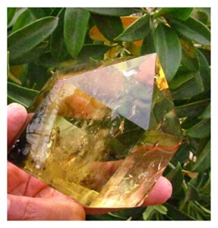 Hand som håller en gul ädelsten framför gröna blad.