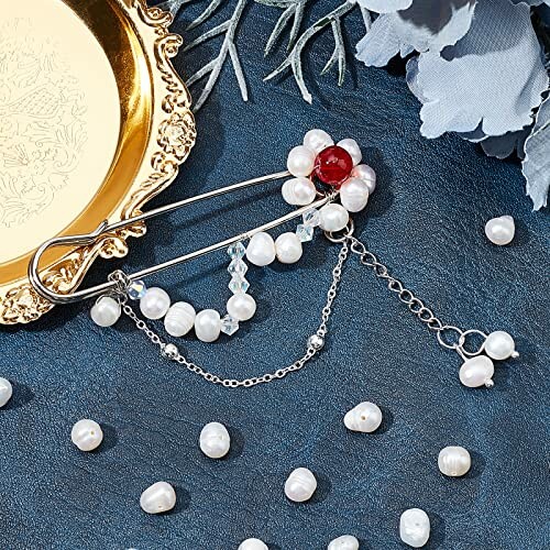 Dekorativ brosch med pärlor och kedjor på blå yta.