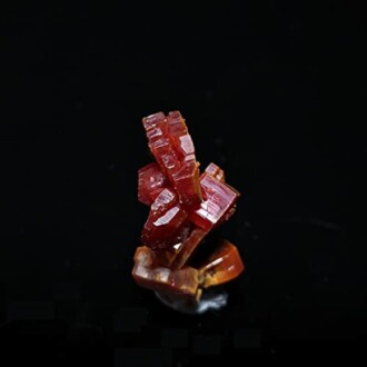 Röd kristallmineral på svart bakgrund.